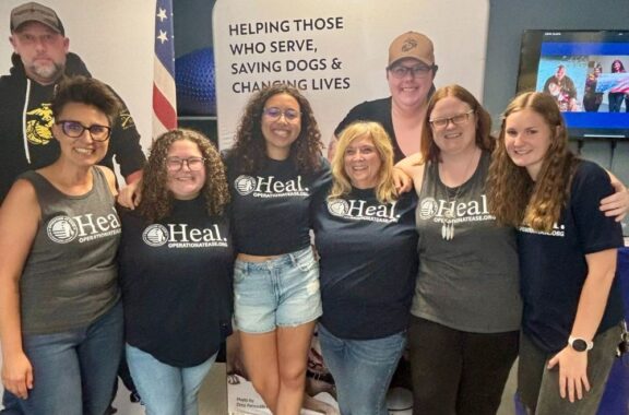 standing arm in arm Operation At Ease team members in Heal t-shirts smiling