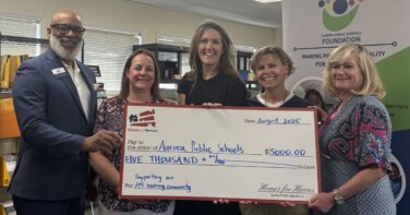 Aurora Public Schools Foundation employees Homes for Heroes specialists with teacher holding big grant check