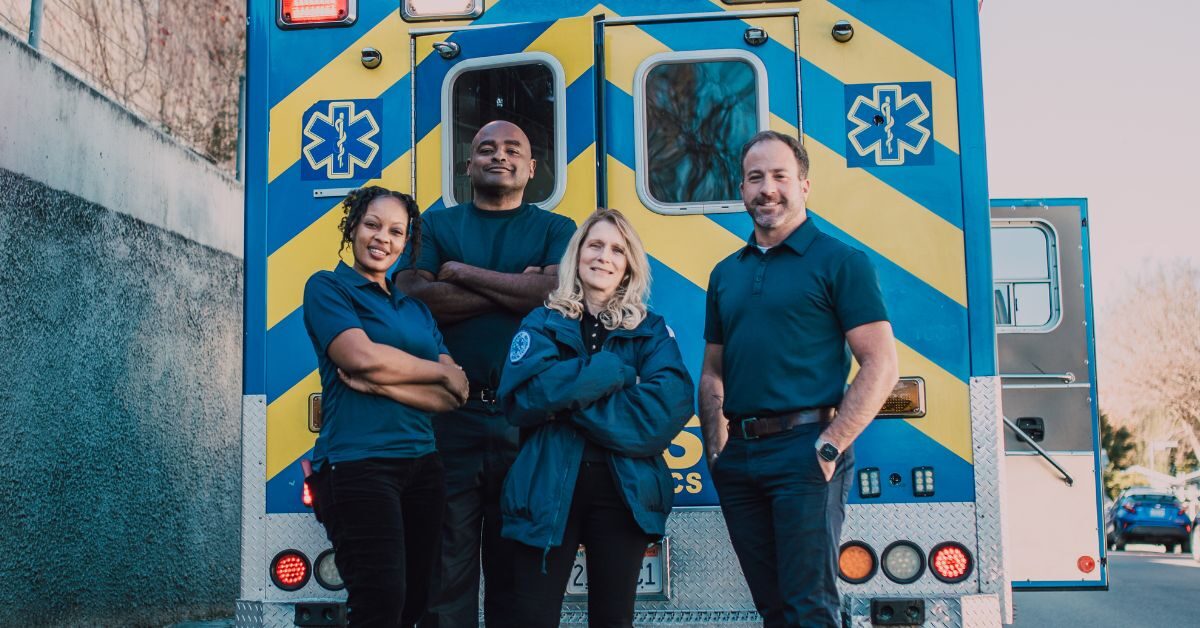 EMS team standing against back end of ambulance smiling in uniform thank you