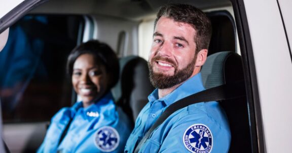 EMT team sitting in ambulance smiling in uniform