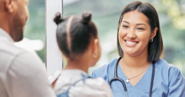 father child patient thanking nurse smiling in scrubs in clinic room