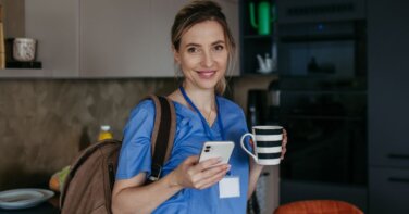 nurse at home in kitchen wearing scrubs holding coffee cell phone carrying backpack smiling