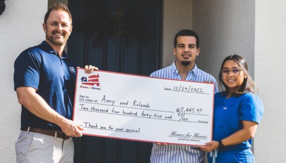 nurse hero couple holding big check outside new home with Homes for Heroes real estate agent specialist