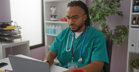nurse sitting at desk recording rounds looking through lab results on laptop