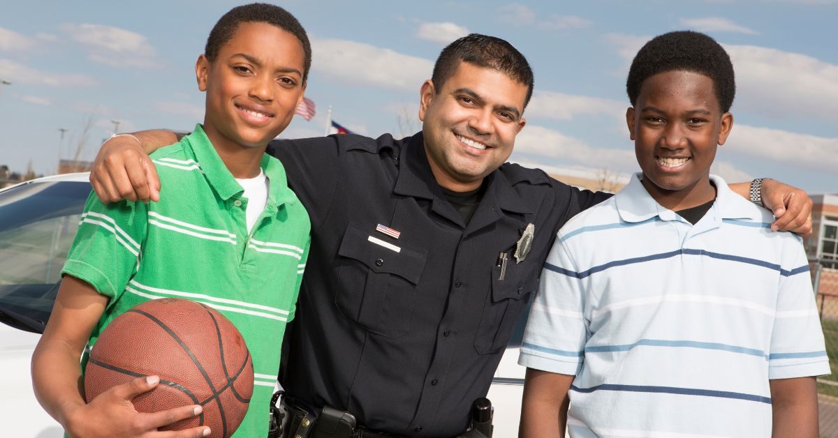 police officer with arms around two young men outside school holding basketball thanking law enforcement