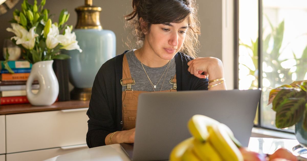 young woman sitting at table researching the Housing Market Trends June 2025 on her laptop from Homes for Heroes